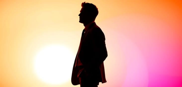 A well-dressed man stands in profile, appearing contemplative against a stunning sunset. The colorful sky features bright orange and pink shades, creating a serene atmosphere.