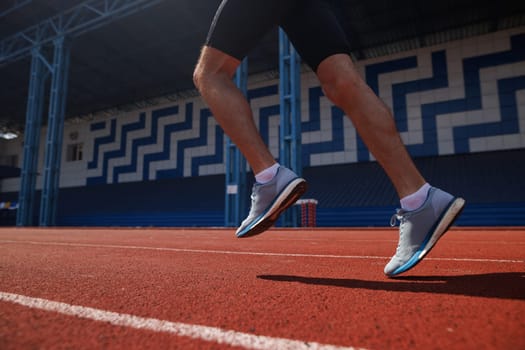 Close-up of a runner's legs in motion on a red track at an outdoor stadium.
