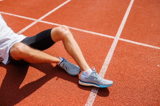 A runner resting on a track after a run, wearing athletic shoes and shorts.
