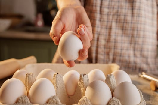 Heart-shaped frying pan for scrambled eggs with broken egg on kitchen table background, cardboard box with eggs and several broken eggshells lie on the ground.