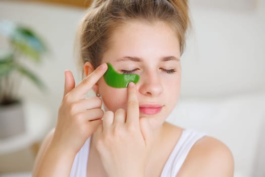 A young woman applying a green under-eye patch to reduce puffiness and dark circles.