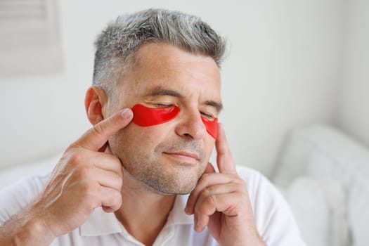 man applying eye patches to face. Wrinkles and facial care at home for men. concept of facial rejuvenation