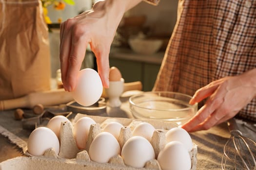 Hand taking chicken egg from box on kitchen table close-up against kitchen atmosphere