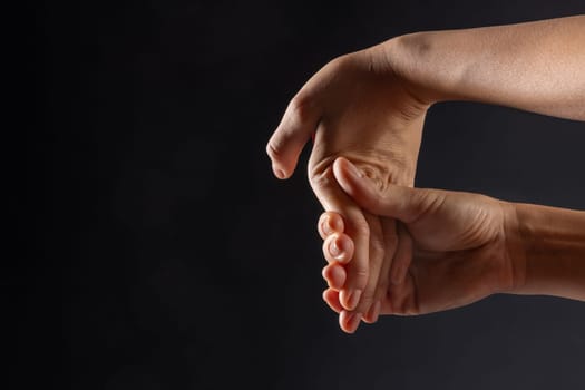 close up of female hands doing wrist stretching on dark background, concept of warm up and wrist fatigue