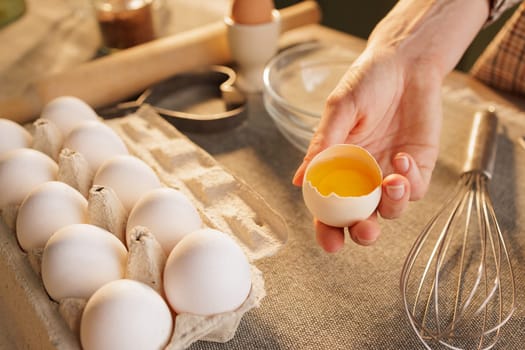 Close-up of female hands holding broken chicken egg on kitchen table background, egg carton, dough preparation