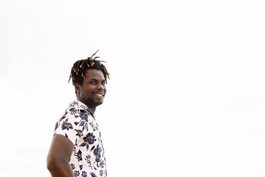 stylish young black man with flower shirt and sky in the background smiling on camera, concept of freedom and lifestyle, copy space for text