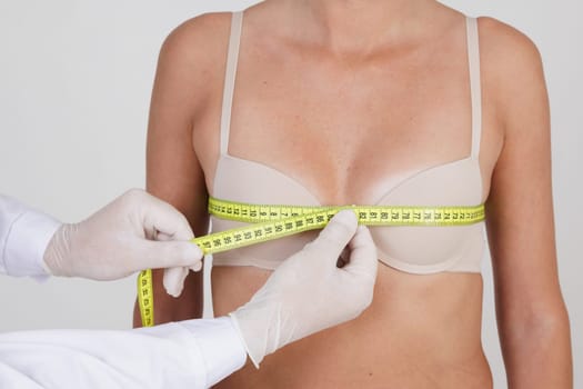 The doctor measures the patient's breast size using a tape measure. concept of increasing breast size