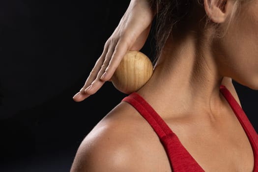 A woman uses a wooden massage ball on her neck to perform a self-massage. She is wearing a red tank top and appears relaxed as she focuses on releasing tension in her muscles. self massage tool