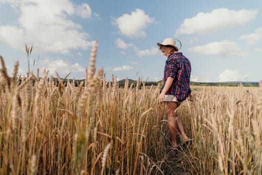A young woman wearing a straw hat walks through a golden field of wheat on a sunny day.