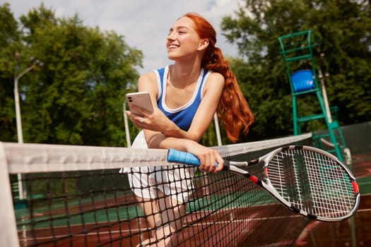 Active, fit and happy female tennis player browsing social media on her phone outdoors on the court. A young female athlete or sportswoman posting her sport training online or on the internet