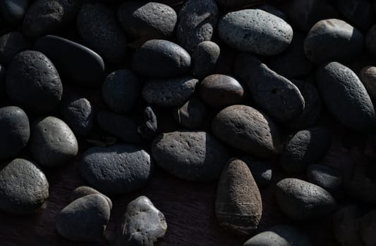 View of Light and Shadow on Black pebbles with Natural Textured Surface. Detail stone cobblestone as a background, Light and Shadow, Space for text, Selective focus.