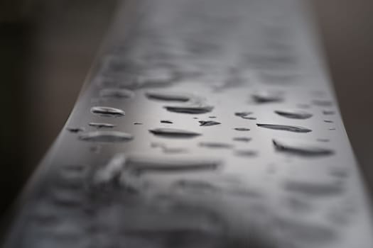 Close up of Rain water drops on the metallic surface. Water droplets caused by rain perched on a stainless steel handle, Natural Pattern of raindrops or dew drops on silver metal background for wallpaper poster and banner design, Selective focus.