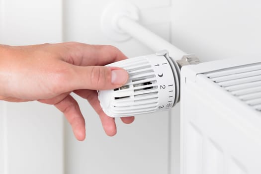 A woman adjusting the temperature on a heating radiator, focusing on saving money and conserving energy. The importance of mindful resource management and cost-effective living during the colder months, actions to manage household expenses