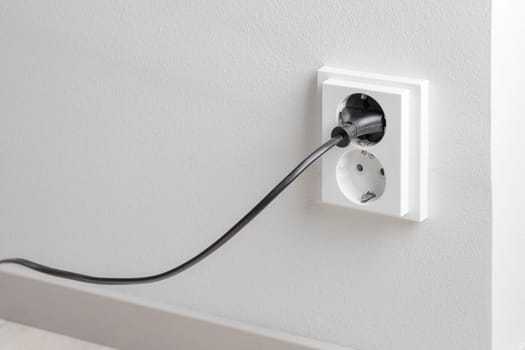 A close-up of a double electrical outlet mounted on a white wall, with a power cord plugged into one of the sockets. Mindful of electricity consumption and energy savings, managing electrical usage efficiently, and reducing waste in everyday life