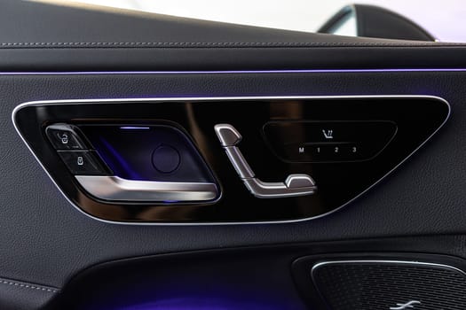 Close-up of a car door interior, showcasing luxurious leather materials and advanced seat adjustment controls, complemented by ambient lighting for a premium driving experience.
