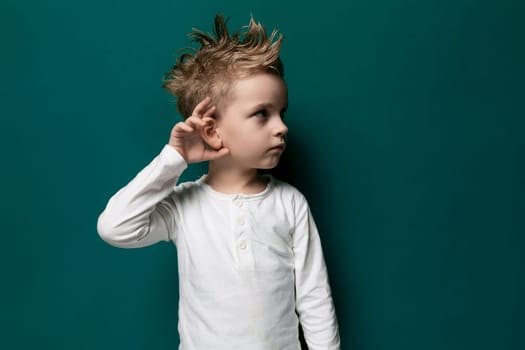 A young boy with a stylish mohawk hairstyle is standing confidently against a vibrant green wall. He is looking directly at the camera, showcasing his unique appearance and bold attitude.