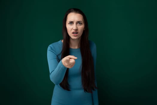 A woman wearing a blue dress is pointing at an unseen object or direction. Her hand is outstretched, indicating she is drawing attention to something specific.
