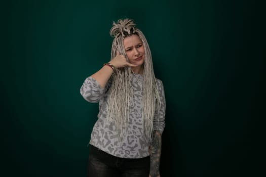A woman with long blonde hair is standing in front of a green wall. She appears confident and poised, looking directly at the camera.