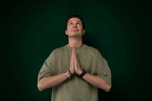 A man is standing upright in front of a solid green wall. He appears to be looking straight ahead with hands by his sides, creating a simple and straightforward composition.