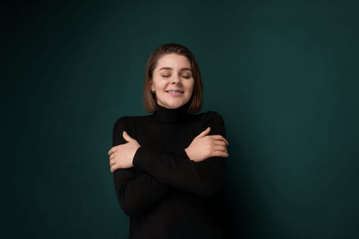 A woman stands with her arms crossed in front of a vibrant green wall. She appears confident and composed, exuding a sense of determination in her posture.