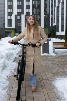 A woman is standing next to a bike in a snowy environment. The scene depicts winter conditions with snow covering the ground and bike. The woman appears to be dressed warmly for the weather.