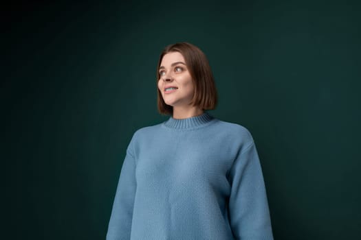 A woman stands confidently in front of a vibrant green wall, her posture strong and determined. The plain wall serves as a simple backdrop to showcase her presence.