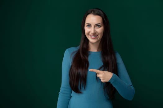 A woman wearing a blue shirt is pointing at an object or direction, indicating focus or interest. She appears engaged and actively communicating a message or drawing attention to something specific.