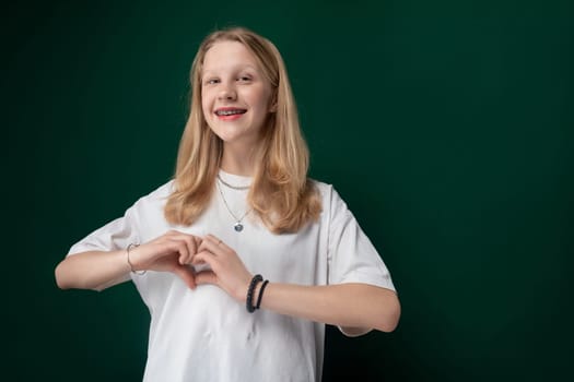 A woman is standing in front of a solid green wall, looking directly at the camera with a neutral expression. She is wearing casual clothing and appears to be posing for a portrait.