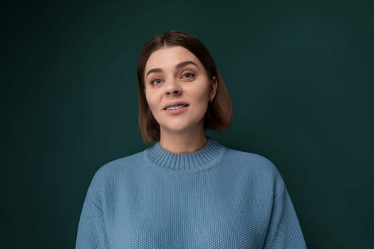 A woman wearing a blue sweater is gazing upwards. Her expression is contemplative as she looks up at something out of frame. The background is simple and nondescript, allowing the focus to be on her.