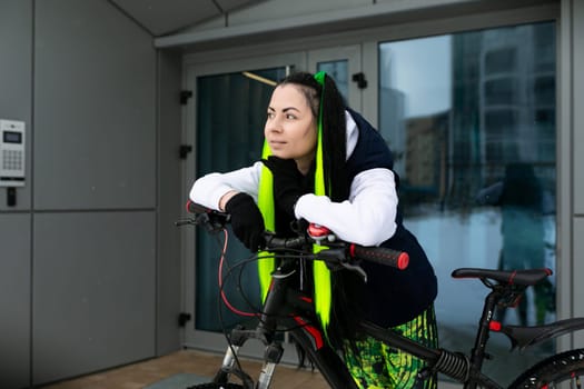 A woman wearing a black jacket and a yellow safety vest is actively pedaling a bicycle on the road.