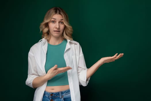 A woman stands in front of a vibrant green wall, holding out her hands in a gesture of openness and invitation. She appears confident and engaged with her surroundings.