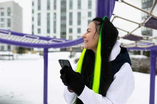 A woman wearing a scarf is seen holding a cell phone in her hand. She appears focused on the screen, possibly texting or scrolling through social media.
