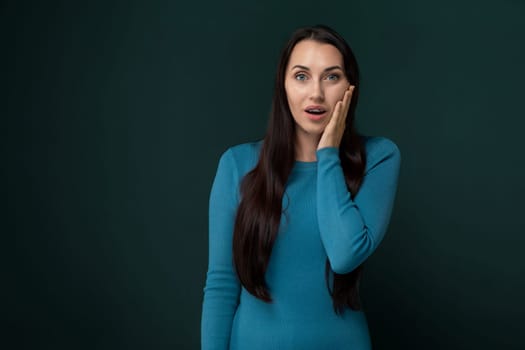 A woman wearing a blue dress is holding her hand to her face.