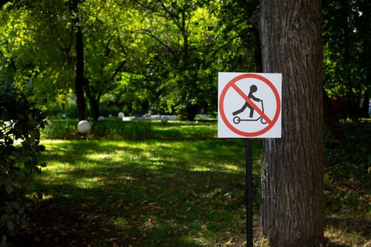 Sign in park with crossed out electric scooter. Ban on riding scooter in public place on street of modern city, rules for transport