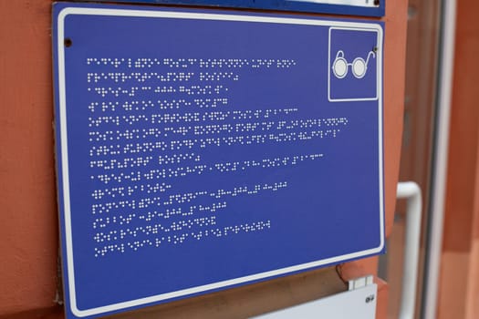 Sign with information in braille text for blind people in front of the building entrance. Accessible environment for people with disabilities, communication in language for people with low vision