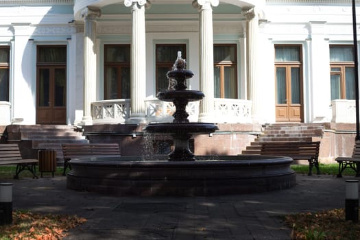 Old fountain in backyard against the background of building facade with columns in street park for people to rest. Pedestrian path near stone fountain