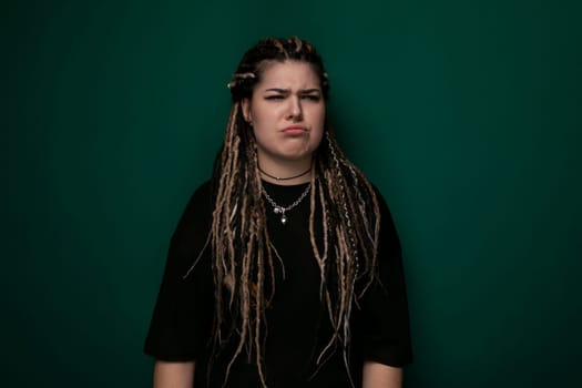A woman with dreadlocks is standing in front of a green wall. She appears confident and stylish, showcasing her unique hairstyle.
