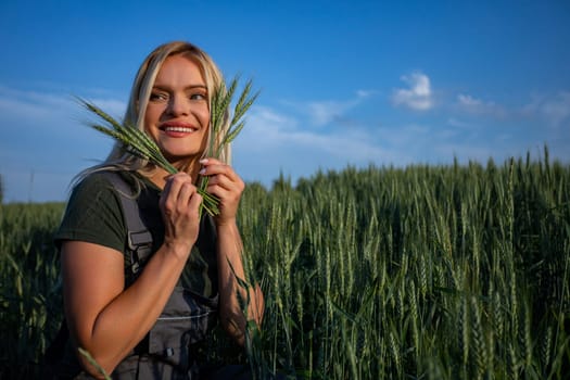 In a sun-kissed wheat field, a female farmer stands, her hands cradling freshly harvested wheat stalks. With a wide smile, she arranges them near her face, revealing her gleaming white teeth. Radiating satisfaction, she celebrates the bountiful harvest. Her sun-kissed skin and blonde hair blend with the golden hues of the landscape. Clad in work attire, she embodies the essence of rural life. The vibrant green color of the wheat stalks contrasts beautifully against the golden backdrop, symbolizing the abundance of nature's bounty. This image captures the joy and pride of farming, where hard work and dedication yield fruitful results. Against the backdrop of the sprawling countryside, the farmer's contentment shines through, a testament to the rewards of agricultural labor. With each stalk held tenderly, she honors the cycle of growth and the timeless connection between farmer and land