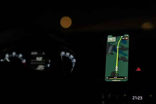 A driver uses a GPS navigation system at night, displaying route information and speed while ensuring a safe journey.