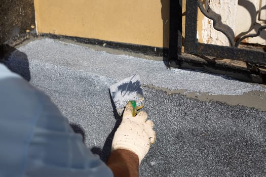 Worker restores the facade of building using spatula. Repairing wall on street, man applies special product for plaster with trowel in dirty work uniform, hard work of builder on street