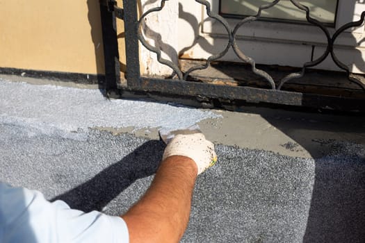Hand of hard worker in protective glove applies putty to facade of building using spatula, builder works on street to restore the building