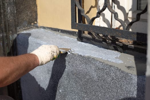 Blue collar applying special solution to wall of building during restoration, using spatula as tool at construction site