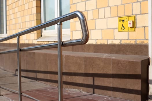 Metal railing is next to yellow sign that says handicap accessible with help button. Ramp for people in wheelchairs at the entrance to building with handrails for assistance