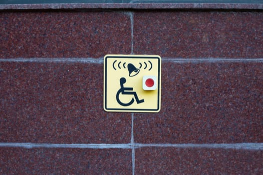 Wheelchair sign next to button to call help on street wall. Accessible area for people with disabilities, moving people in wheelchairs in modern city