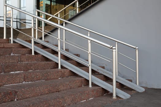 Metal ramp with handrails for grip for access to building on staircase for people on wheelchair. Accessible environment for people with strollers and wheelchair for rolling up steps