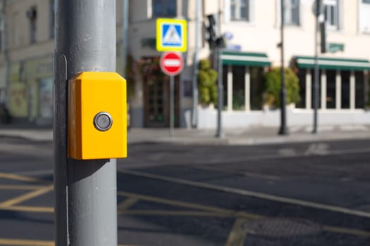 Yellow panel on pole with button for pedestrian to change the traffic light while crossing the road at an intersection in city