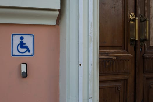 Modern button to call help for people in wheelchair at entrance to old building. Restoration of old building with creation of modern amenities for people with disabilities. Wheelchair sign near door of building