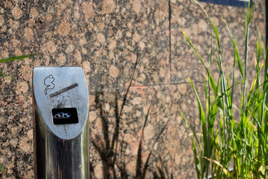 Modern ashtray on street in smoking area, metal pole with compartment for disposing of cigarettes, health problems of smoking of the population people on city street in public place