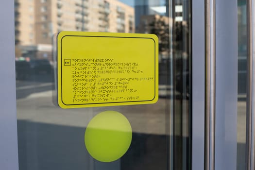 Yellow sign with black writing braille text. The sign is in language for blind people. Means of communication with people with disabilities on sign on door on entrance to the building