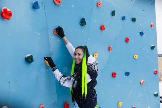 A woman is seen ascending the side of a climbing wall, using her strength and skill to reach the top. The wall is textured with grips and holds for support as she makes her way up.